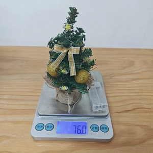 Mini decorated Christmas tree with lights weighing 76.0g on a digital scale