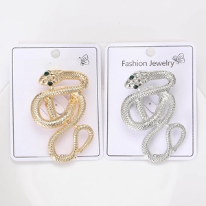 Detail of snake brooch featuring textured scales and green crystal eyes on card