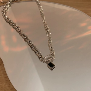 Stainless steel chain necklace with black rectangular gemstone pendant on mirror surface