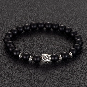 Macro detail of matte black beads and antique silver owl charm on a leather background
