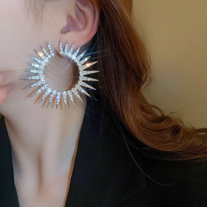 Close-up of sparkling silver rhinestone hoop earrings in a sunburst gear design on model