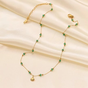Close-up of gold starfish shell necklace with green beads on silk background