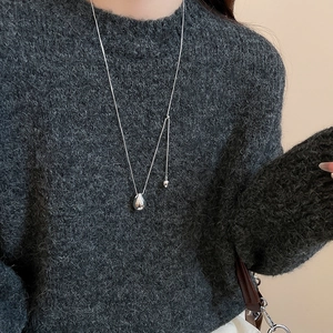 Close-up of a minimalist silver teardrop pendant necklace on a grey knit sweater
