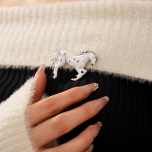 Macro view of vintage horse brooch with white enamel and rhinestones on knitwear