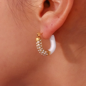Macro shot of U-shaped gold plated earrings with white enamel and micro-inlaid zircons