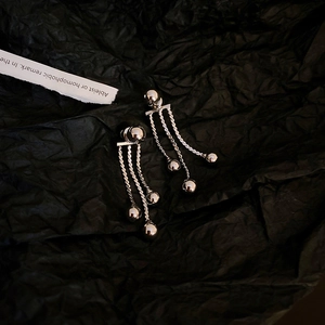 Detail of silver metal fringe earrings with spherical tassels on a textured background