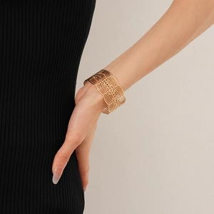 Détail de bracelet doré à motif dentelle ajourée et design géométrique sur le poignet