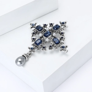 Close-up of silver baroque cross brooch with blue gemstones and hanging gray pearl