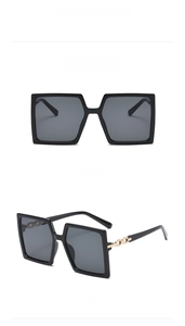 Detail of black square oversized sunglasses with gold chain link on temple and grey lenses