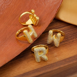 Dettagli di anelli in rame placcati oro con zirconi incastonati sulle lettere H, W e R