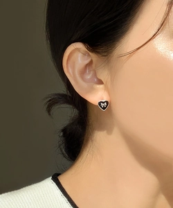 Close-up of model wearing black heart stud earrings with silver bow detail