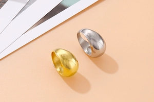 Polished gold and silver teardrop rings with smooth mirror finish on warm background