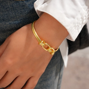 Detail of 18K gold plated knotted open bangle worn on wrist with a casual stylish outfit