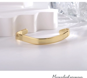 Detailed view of an irregular wave-shaped gold brass bangle on a clean minimalist surface