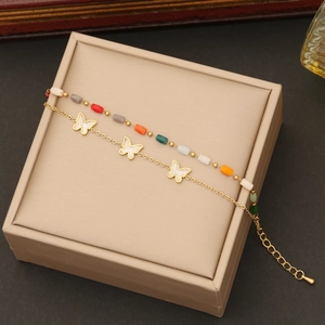 Macro shot of double-layer gold chain with white butterfly charm and colored beads on a box