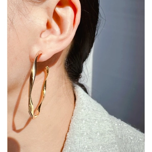 Golden oversized twisted hoop earrings in wavy metal design for a trendy fashion statement