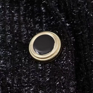 Detail of a decorative black and gold button on textured tweed blazer fabric