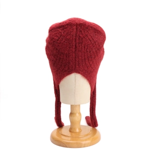 Dettaglio del cappello in maglia di lana rosso scuro con paraorecchie e nastri lunghi invernali