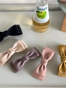 Flat lay of five silky bow hair clips in black, beige, purple, pink, and yellow colors