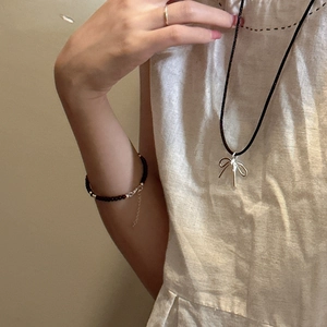 Silver bow pendant necklace with black cord and beaded bracelet set on model