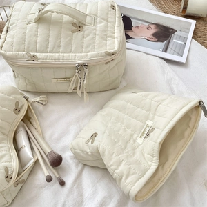Detailed macro view of quilted rabbit embroidery and brand label on cream makeup pouch