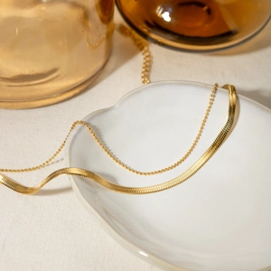 Elegant 18K gold-plated double-layer snake and bead chain anklet on a white ceramic dish