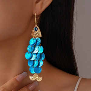 Detailed view of fish-shaped gold earring with blue shell scales and evil eye charm