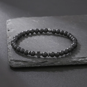 Macro detail of black lava stone beads and metal cross charm on a dark rock surface