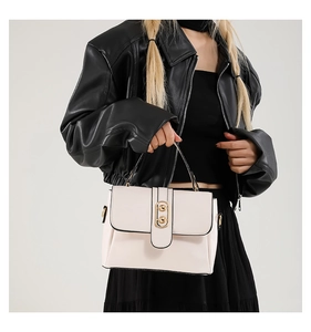 Chic cream-white crossbody bag with gold round buckle shown on black leather outfit