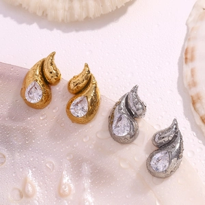 Macro shot of gold and silver teardrop zircon earrings with water drops on a shell