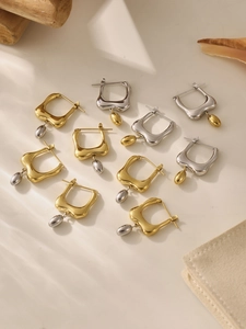 Polished gold and silver geometric hoop earrings with drop pendants on cream background