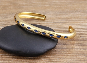 Macro detail of 18k gold plated C-shaped bangle featuring marquise-cut blue zircon stones
