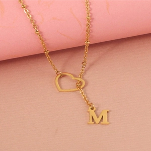 Gold stainless steel necklace with hollow heart pendant and letter M on pink texture