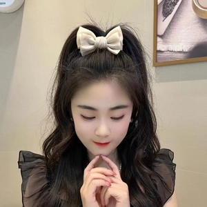 Detail showing a cream bow hair claw clip styled on a woman's bun hairstyle