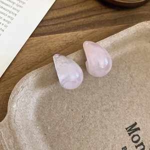 Close-up of pink teardrop resin earrings displayed on a vintage paper tray background
