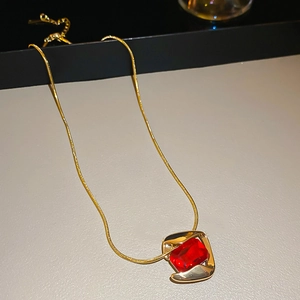 Close-up of a gold snake chain necklace featuring a vintage red gemstone pendant