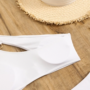 Detail of white ribbed bikini fabric with decorative gold metal ring on wooden background