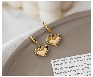 Detailed close-up of glossy gold heart pendant earrings resting on a matte ceramic tray