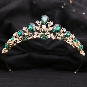 Detail of a baroque crown with emerald green gems and rhinestones on a black background