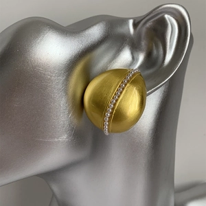 Macro di orecchini a goccia in oro opaco con perle indossati su orecchio di modella
