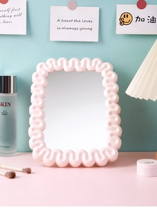 Detail of pink wave-edged vanity mirror on a dresser with makeup accessories