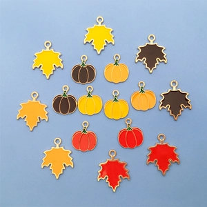 Flat lay of colorful enamel maple leaf and pumpkin charms with gold metal bases for DIY