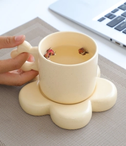 Close-up of a cream ceramic mug with cloud handle and floral saucer in a cozy office setting