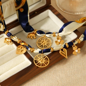 Silk scarf necklace with gold sun, elephant, heart, and clover charms in a wooden box