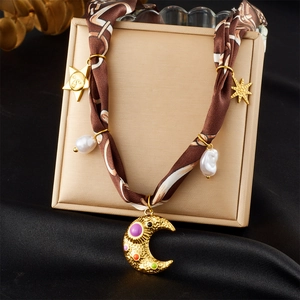 Détail d'un collier en ruban de soie avec breloques lune, soleil dorés et perle baroque
