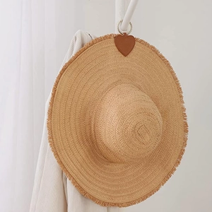 Close-up of a straw sun hat featuring a heart-shaped leather patch and metal hook detail