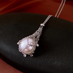 Detailed close-up of a large white pearl pendant with zircon mesh wrap on black velvet