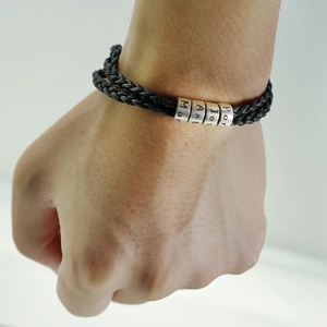 Gros plan d'un bracelet en cuir tressé noir avec perles métalliques gravées au poignet