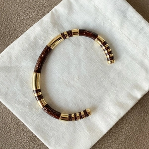 Detail of a C-shaped gold metal cuff bracelet with brown marble resin on a linen pouch