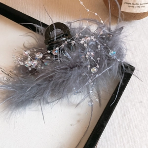 Detailed close-up of a dark grey feather hair claw clip with colorful beads and ostrich feathers